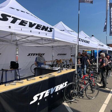 Gazebo per eventi 3x3m bianco personalizzato con logo Stevens bikes a evento sportivo di bicicletta con pareti laterali e pareti laterali a mezza altezza nere con banconi