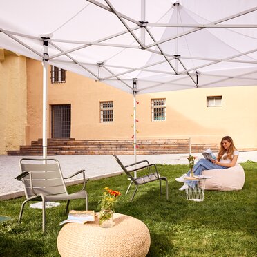 Gazebo Ecotent bianco 6x4m su gairdino davanti alla biblioteca di Bressanone utilizzato outdoor ripara dal sole una studentessa bionda che legge 