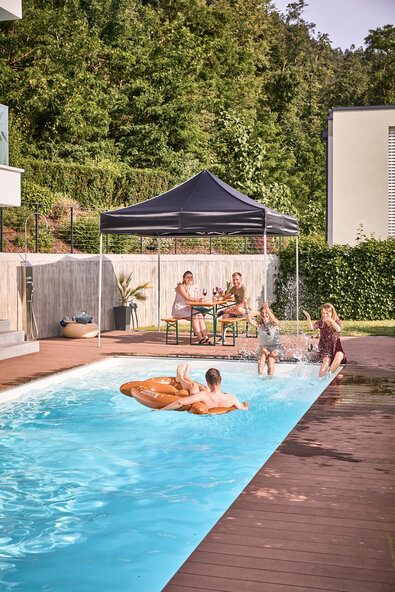 Il gazebo pieghevole nero si trova a bordo piscina nel giardino. Gli amici si siedono all'ombra e fanno una festa in piscina e in giardino.