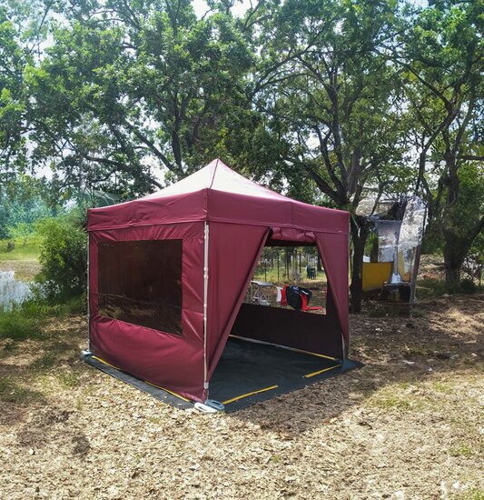 Gazebo pieghevole 3x3 da campeggio color bordeaux con teli laterali e pavimento in pvc in un camping