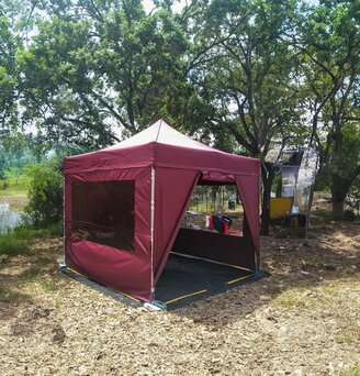 Gazebo pieghevole 3x3 da campeggio color bordeaux con teli laterali e pavimento in pvc in un camping