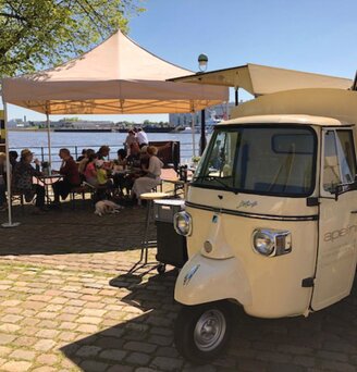 Gazebo 4x4 ecru Apellini copre gli ospiti che mangiano vicino al fiume. In primo piano un'ape beige.